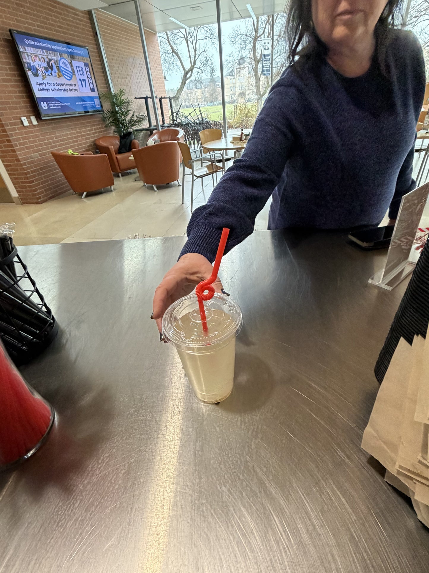 Extra flexible red art straw twisted in a drink cup held by a person at a modern cafe table