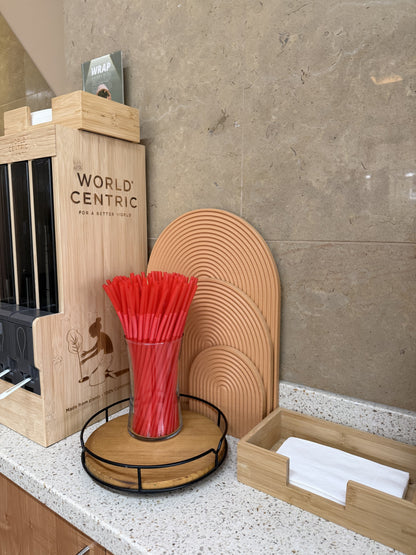 Red extra flexible art straws in a glass on a kitchen counter with wooden organizers and beige background wall